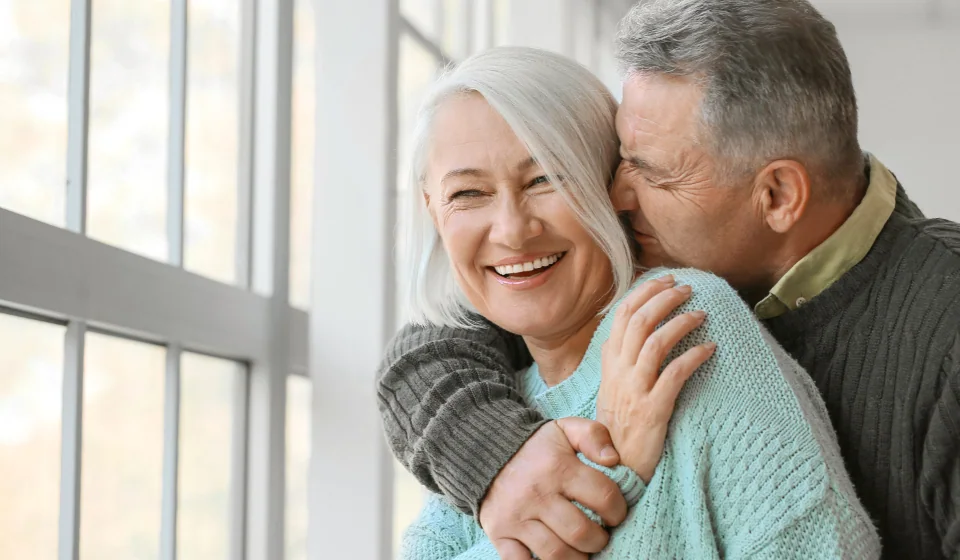 Older couple laughing together by a bright window at home
